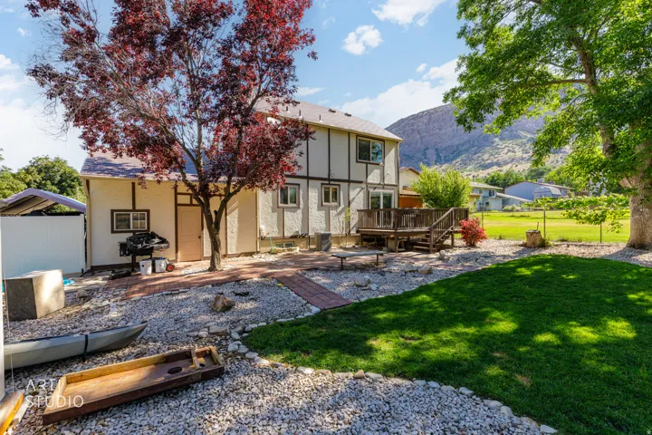 Spacious backyard featuring a wood deck, red brick paver pathways, established trees, and a manicured lawn area