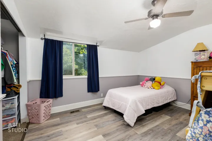 Room featuring wood-finish flooring, a contemporary ceiling fan with integrated lighting, and a window with dark curtains
