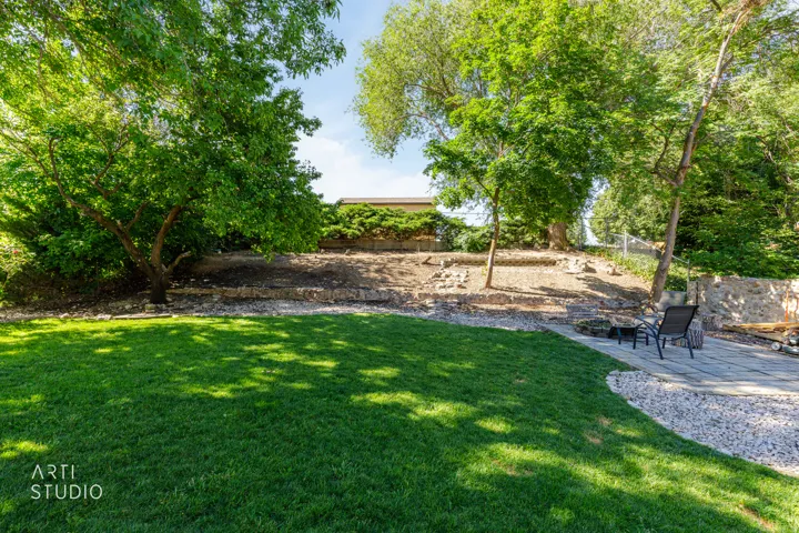 Expansive outdoor area featuring a manicured lawn, established trees, and a stone retaining wall