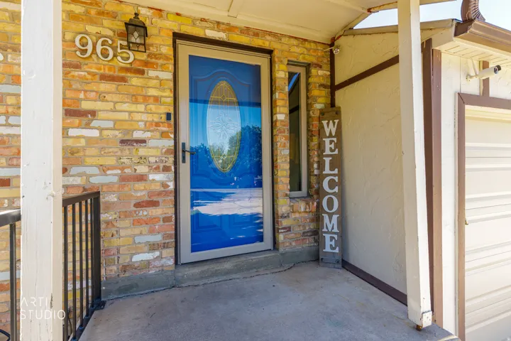 Entryway featuring a multi-toned brick facade, a blue front door with an oval glass insert, a side window, and a concrete porch floor