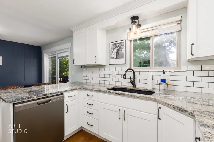 Bright, renovated kitchen featuring white shaker-style cabinetry, subway tile backsplash, and speckled granite countertops