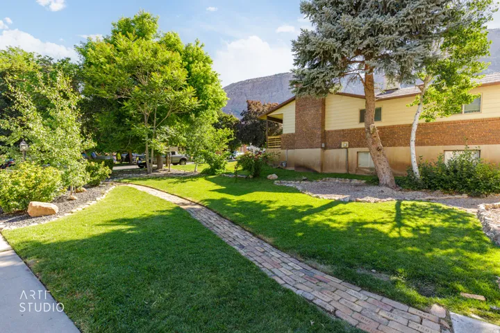 Brick paver pathway with manicured lawn, established trees, and mature landscaping