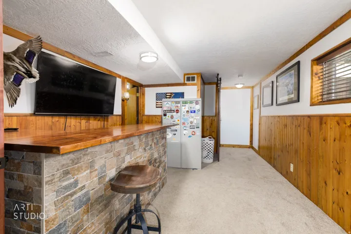 Recreational room featuring a stone-faced bar with a wood-finish countertop, wood paneling, and carpet flooring