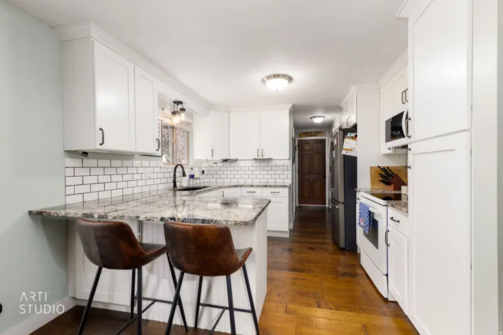 Galley kitchen featuring white cabinetry, subway tile backsplash, stainless steel appliances, and a quartz countertop with waterfall edge