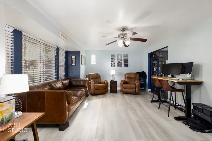 Spacious living area showcasing rich cognac leather seating, light wood-finish flooring, and abundant natural light from large window treatments
