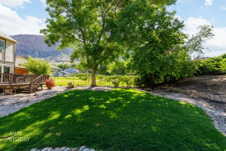 Expansive backyard featuring a lush lawn, mature shade trees, a multi-level wooden deck with railings, and a gravel-lined pathway