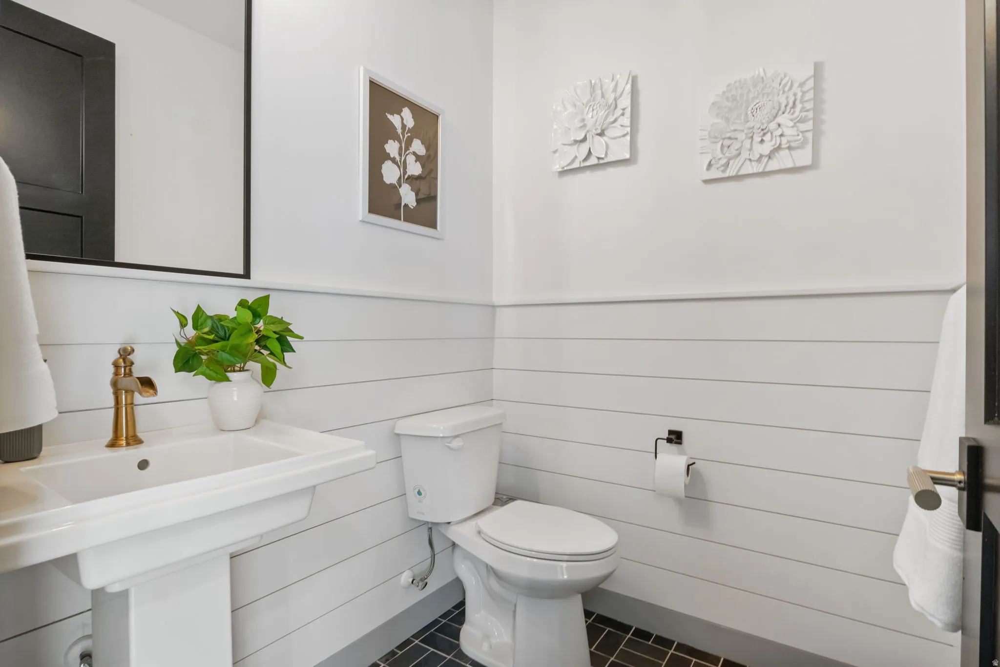 Bathroom with a pedestal sink, brass faucet, and black-framed mirror