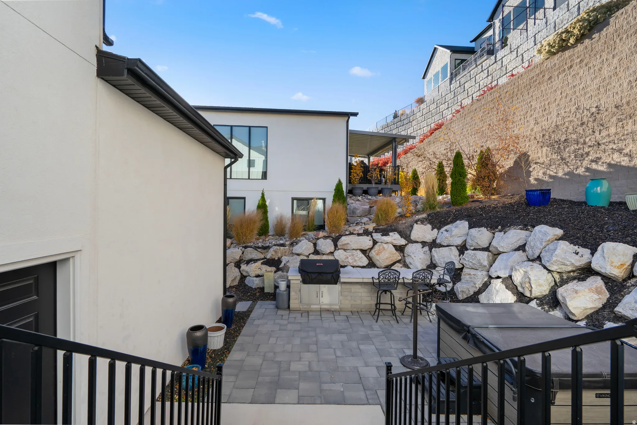 Exterior patio featuring stone pavers, a built-in outdoor grill, and a terraced rock garden with mature plantings