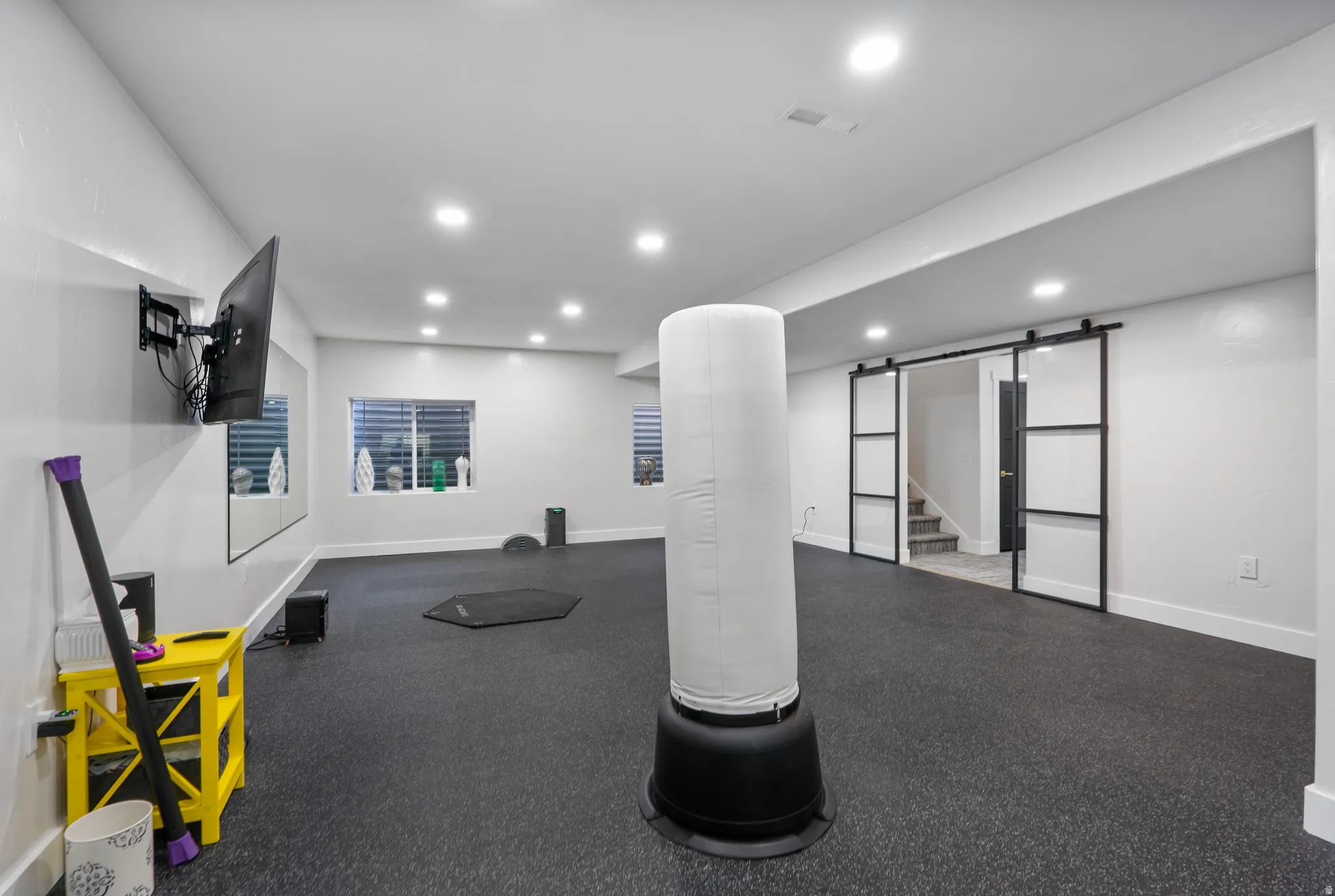 Expansive room featuring black rubber flooring, recessed lighting, and wall-mounted television