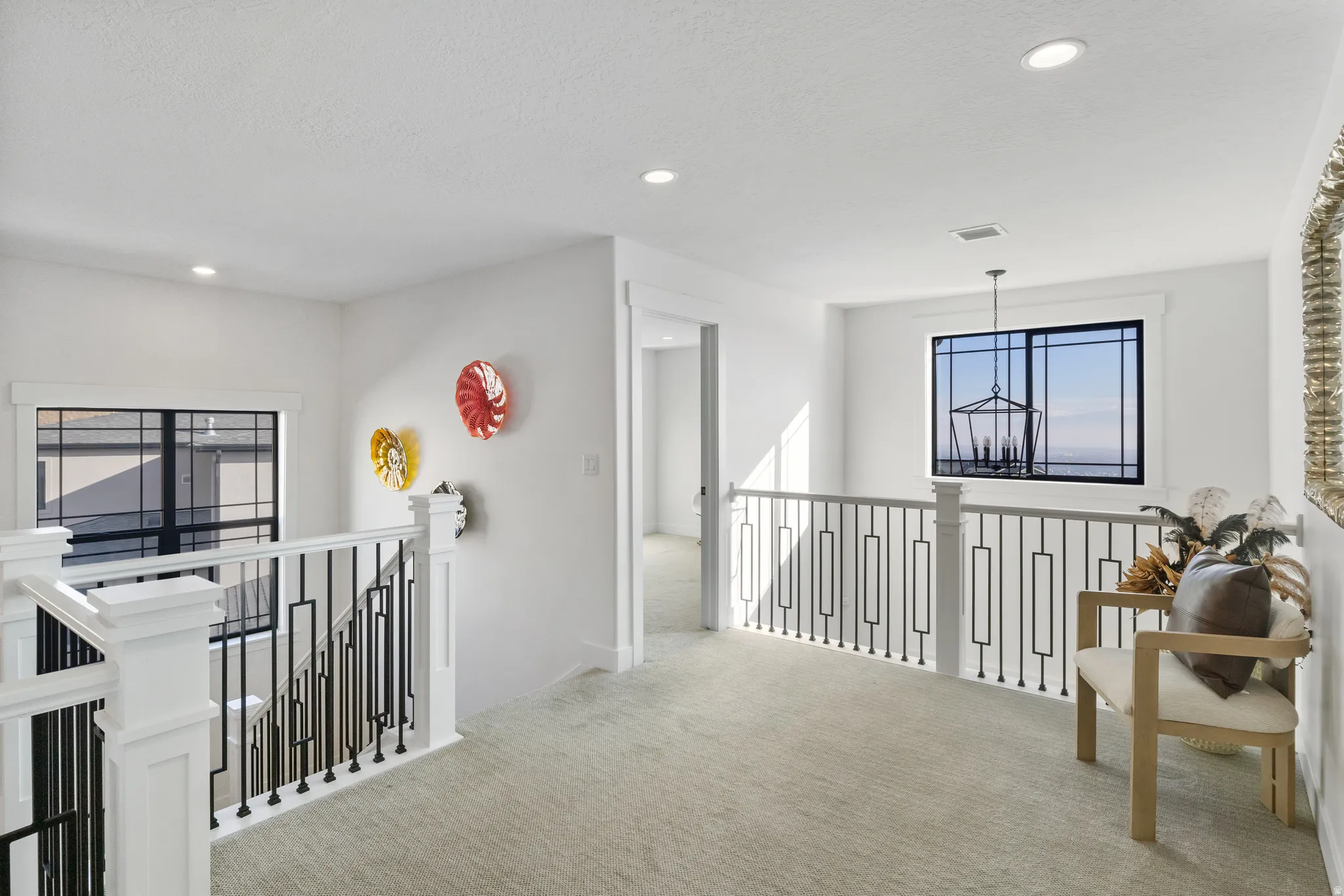 Upper-level landing featuring a white railing with black metal balusters, recessed lighting, and light gray carpeting