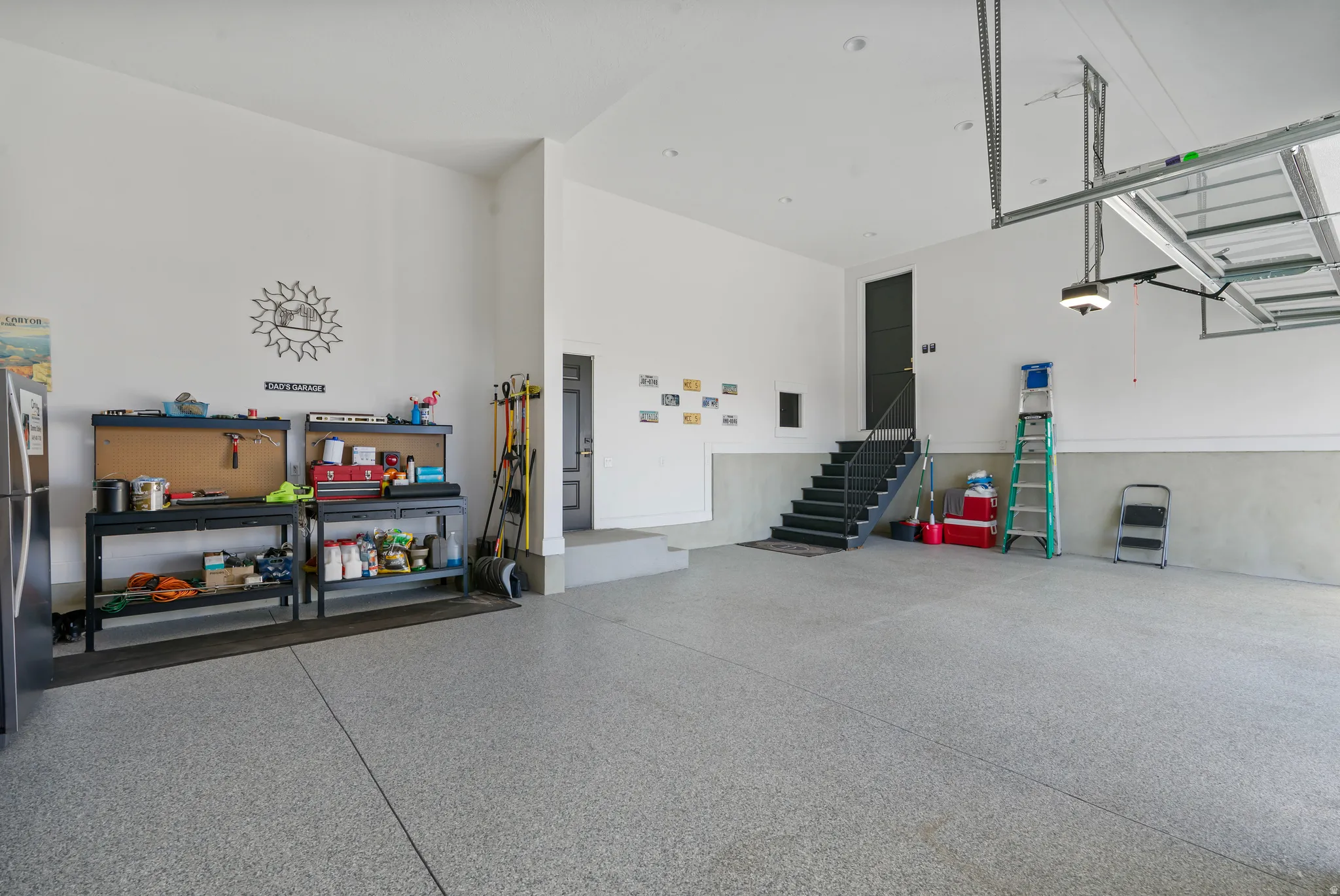 Spacious garage with epoxy flooring, high ceilings, a built-in staircase with dark treads, and a modern overhead garage door system