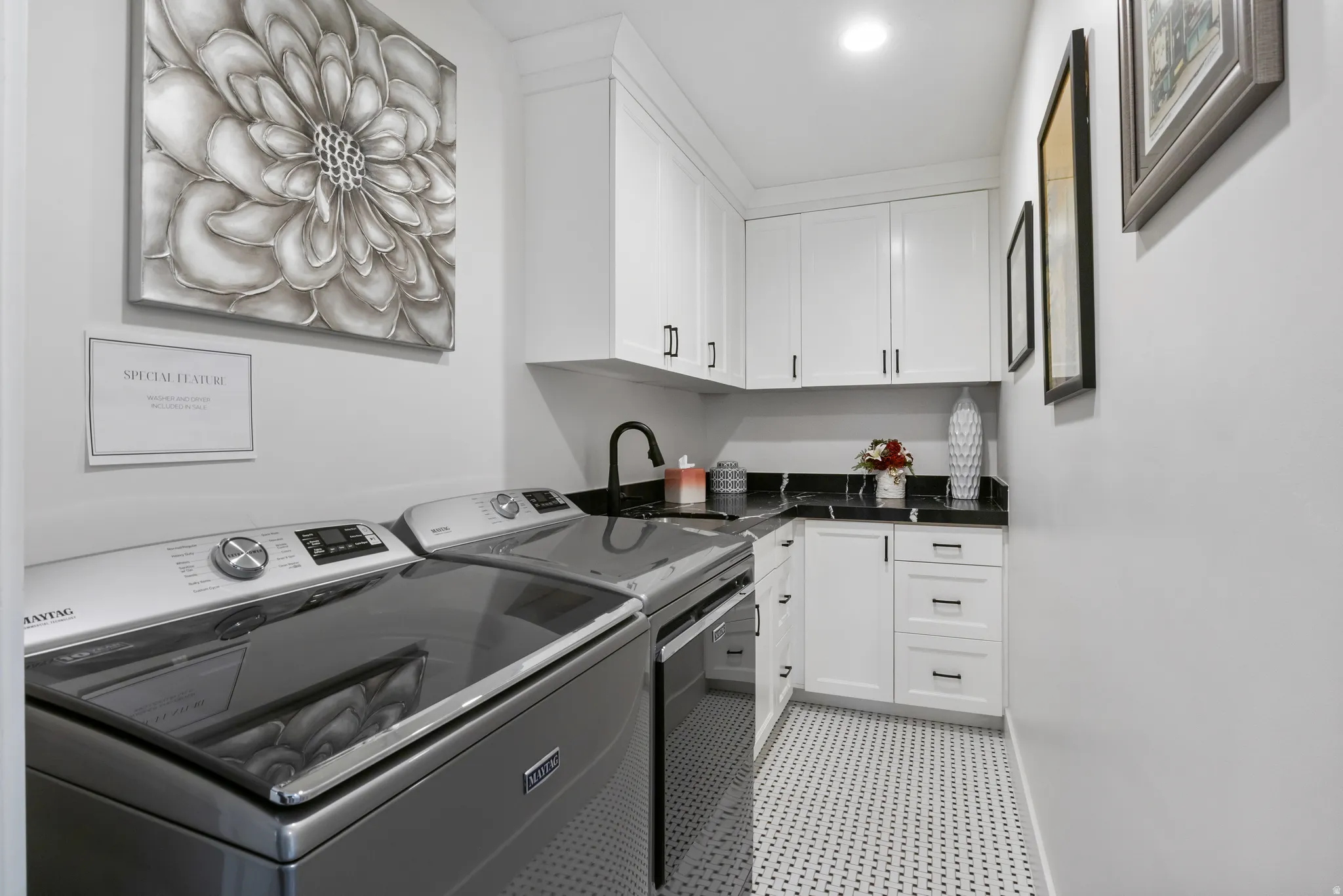 Dedicated laundry space featuring white shaker cabinetry, dark countertops, black fixtures, and mosaic floor tile