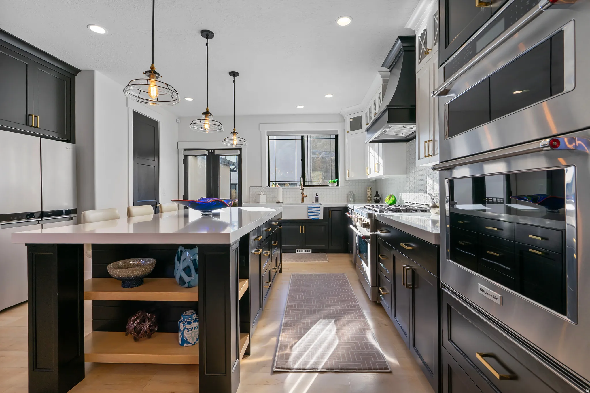 Spacious kitchen featuring a large central island with a light-toned countertop, dark cabinetry, stainless steel appliances, pendant lighting, and light wood-finish flooring