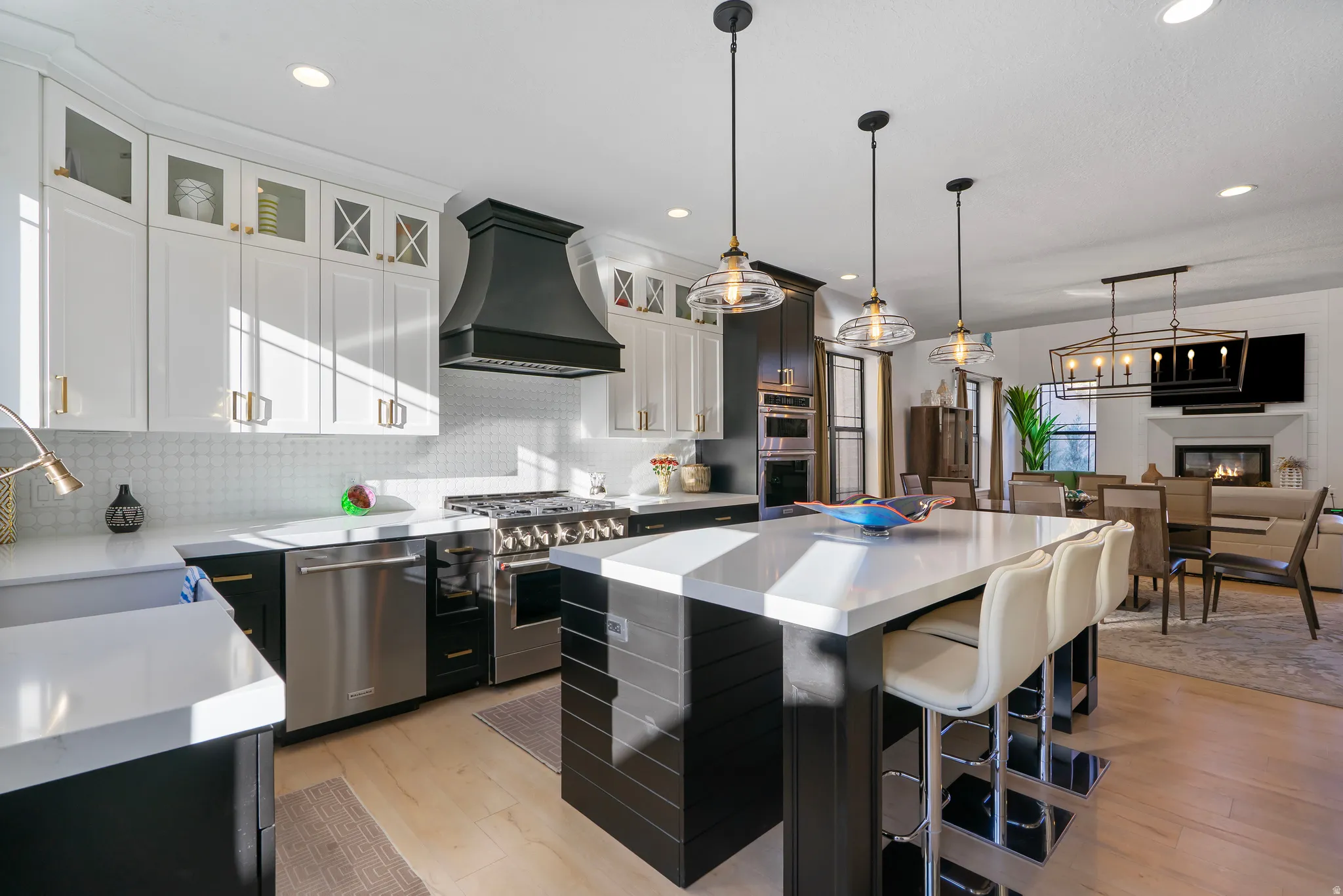Open-concept kitchen featuring an oversized island with countertop seating, stainless steel appliances, a custom range hood, two-tone cabinetry, and wood-finish flooring