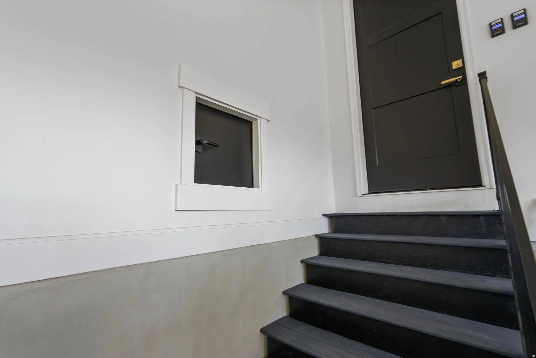 Black painted wooden stairs with a coordinating metal handrail leading to a dark paneled door featuring brass hardware