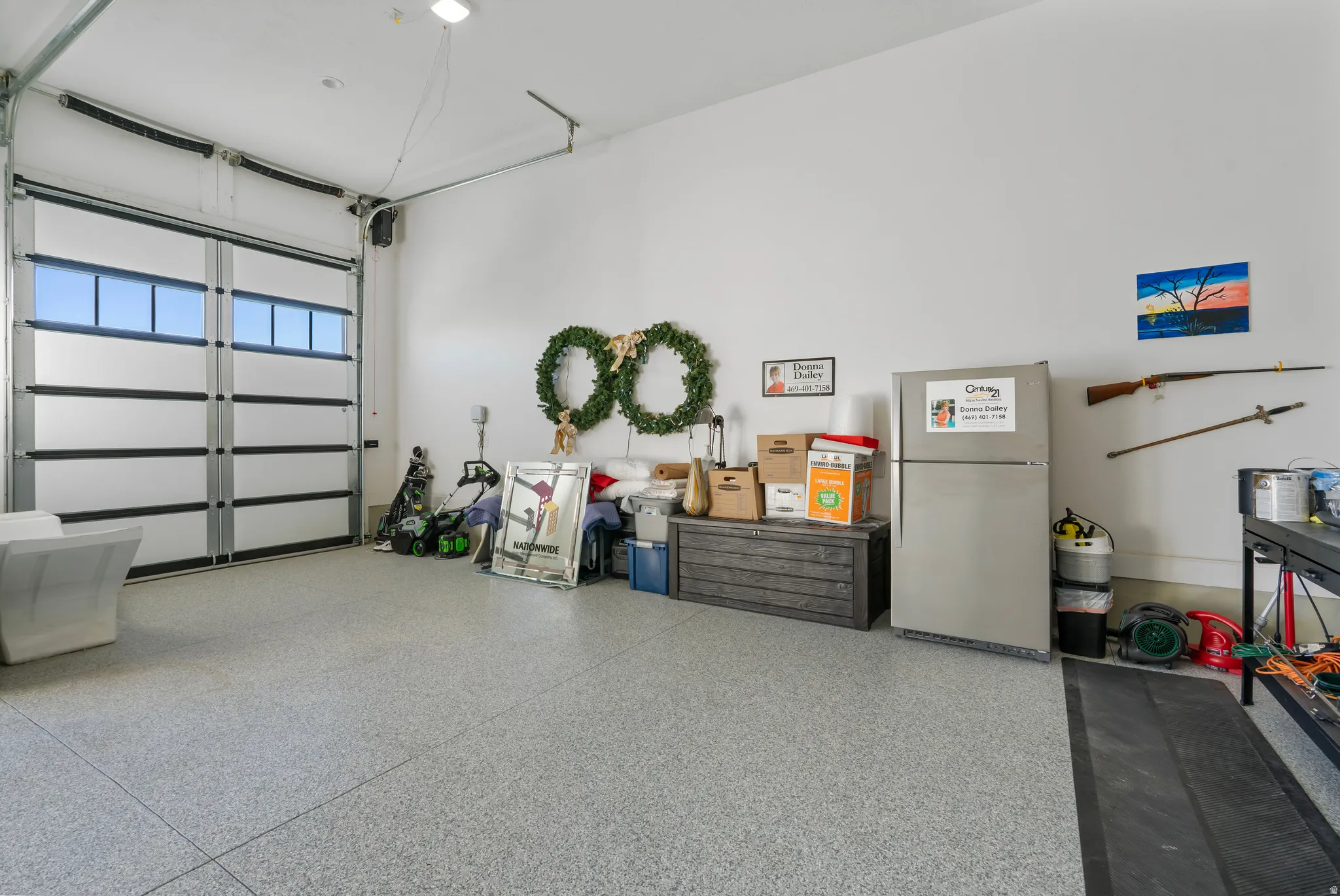 Garage featuring a sectional overhead door with upper horizontal window panels and a light gray epoxy flooring
