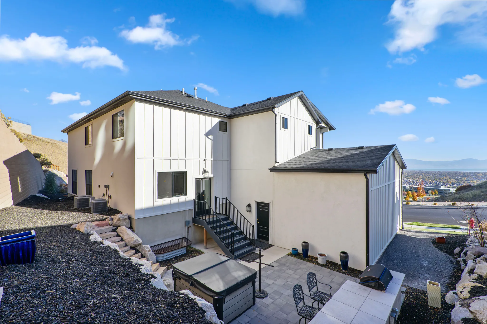 Multi-level exterior featuring white siding and black trim, a lower-level patio with pavers, a hot tub, and a built-in outdoor counter