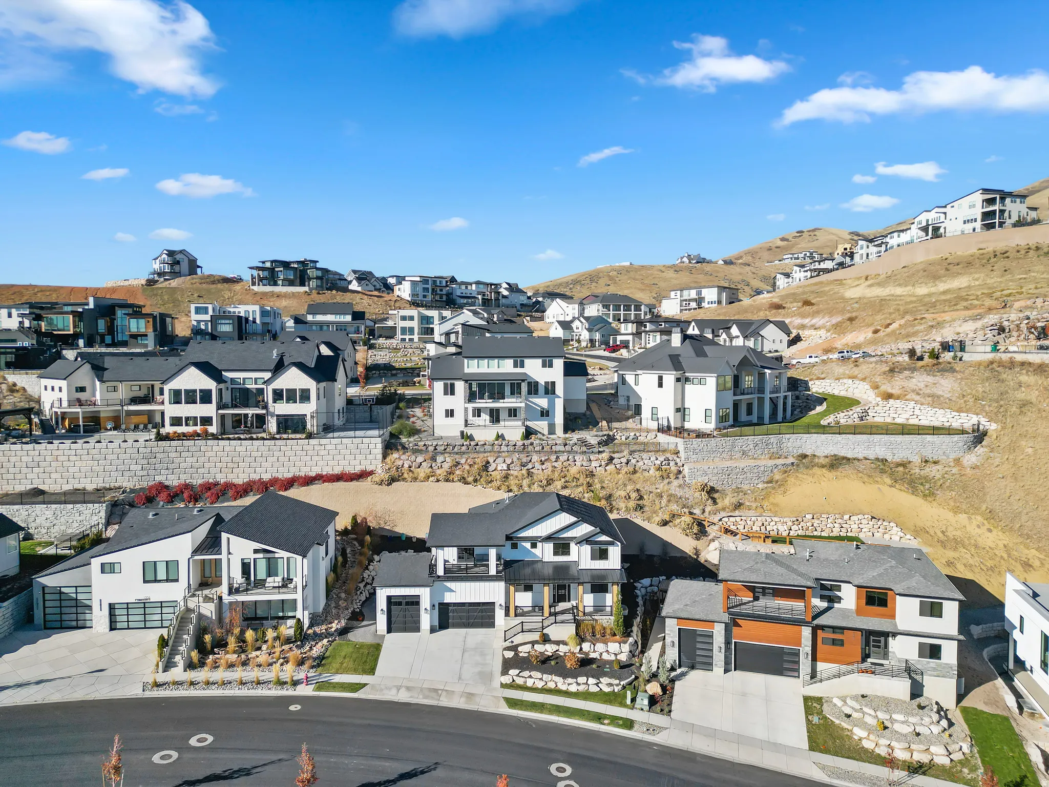 Contemporary hillside residences featuring varied architectural designs, attached garages, and engineered retaining walls