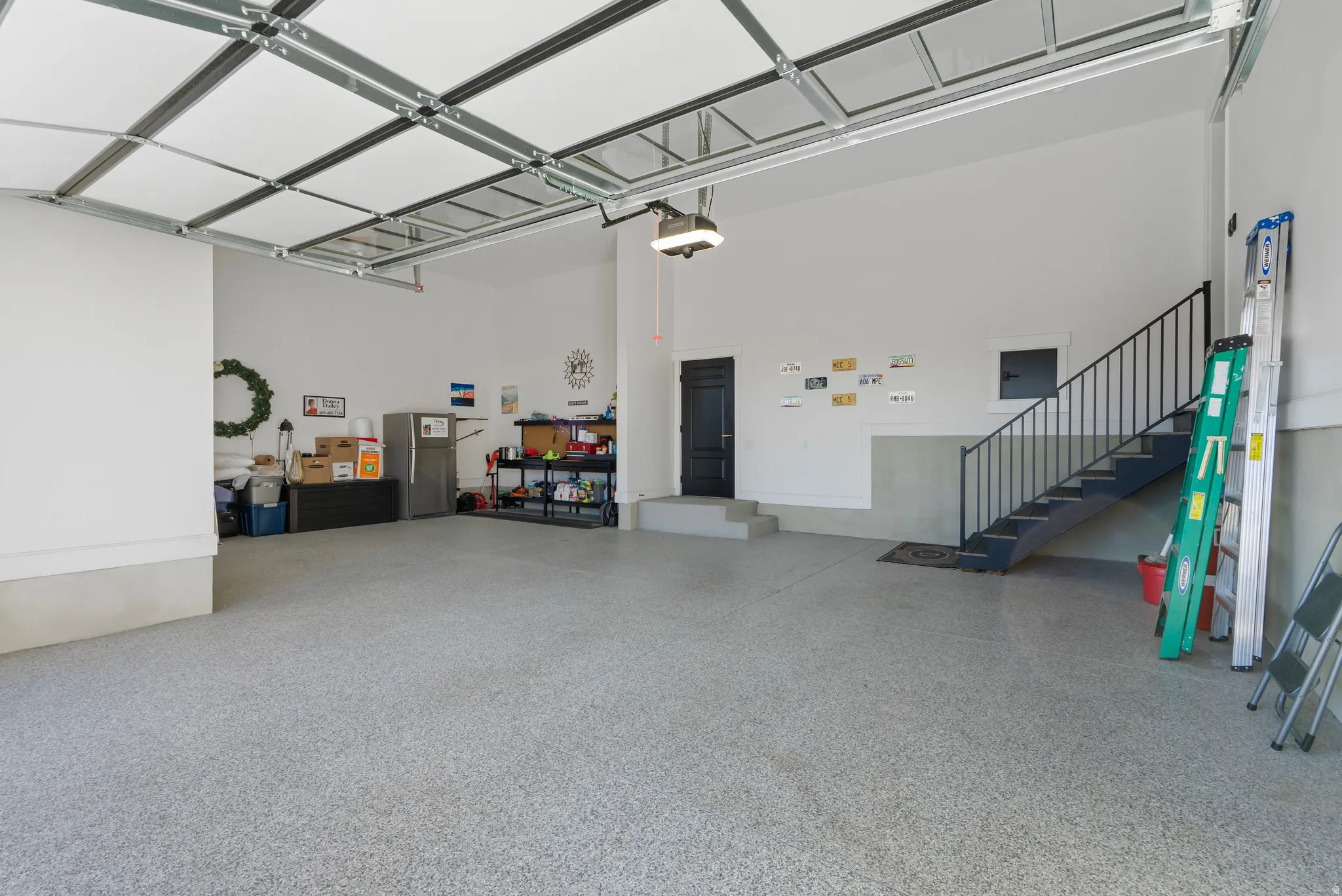 Spacious garage featuring a durable epoxy floor, an integrated staircase with wrought iron railing, a pedestrian door, and high ceilings