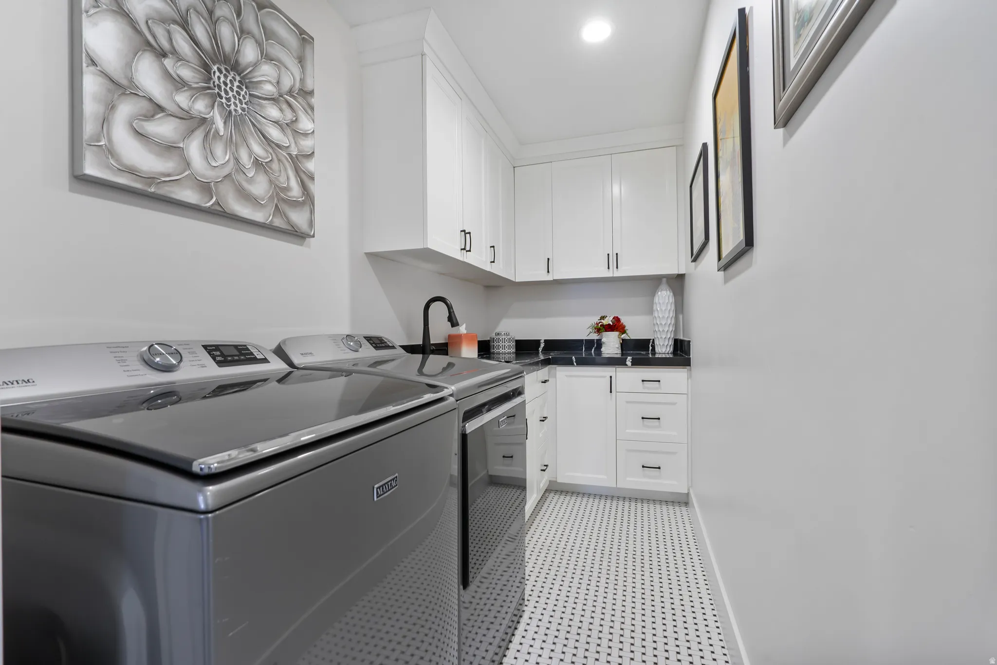 Dedicated utility space featuring white cabinetry, dark countertops, black hardware, a built-in sink with a matte black faucet, and patterned mosaic tile flooring