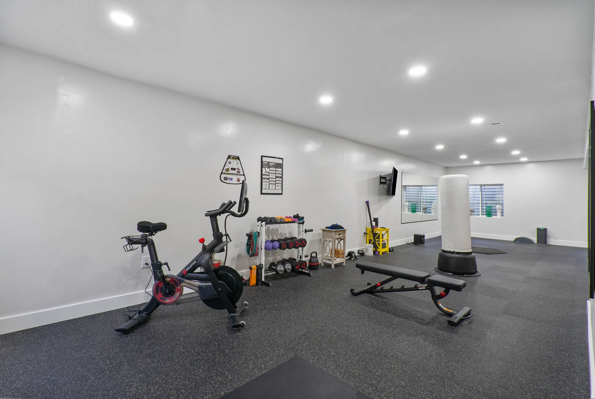 Dedicated fitness space featuring impact-absorbing flooring, multiple recessed lighting fixtures, and light-filtering window treatments