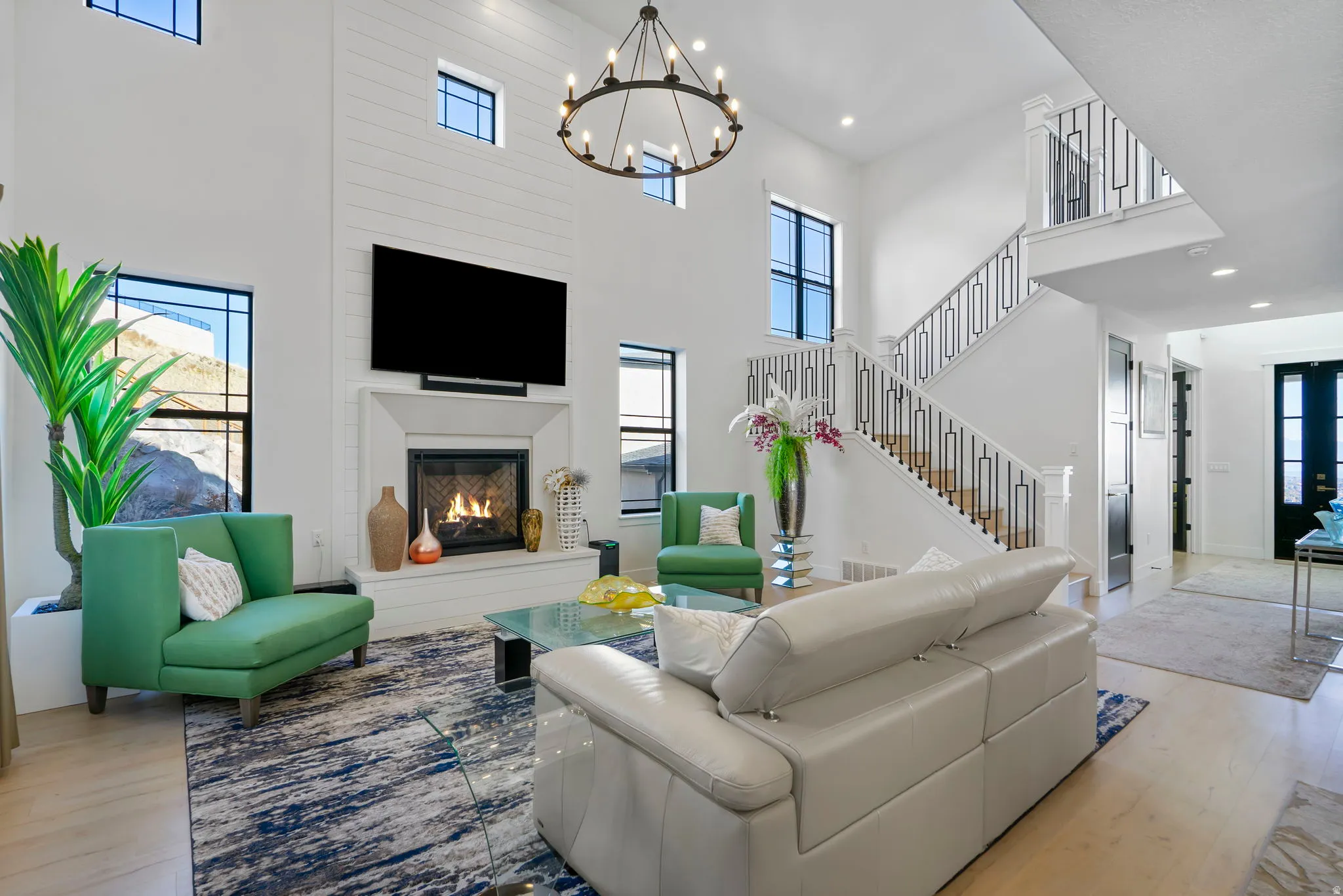 Two-story living area featuring a central fireplace with shiplap accent wall, a grand staircase with wrought iron railing, black framed windows, and light wood-finish flooring