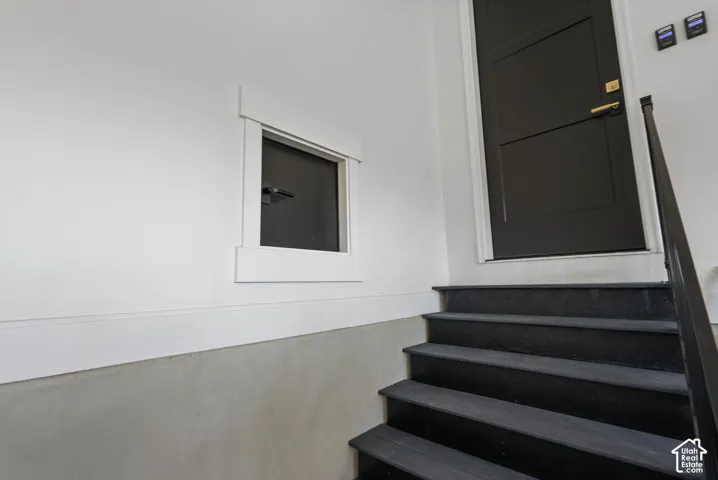 Black painted wooden stairs with a coordinating metal handrail leading to a dark paneled door featuring brass hardware