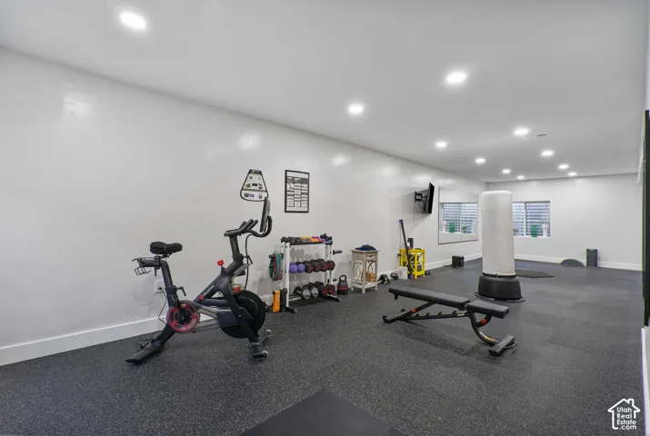 Dedicated fitness space featuring impact-absorbing flooring, multiple recessed lighting fixtures, and light-filtering window treatments