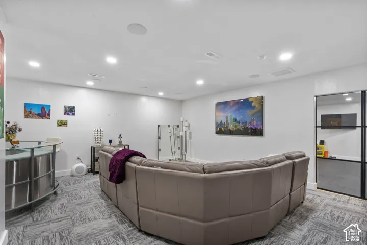 Spacious entertainment area featuring recessed lighting, a modern glass-top bar, and gray patterned flooring
