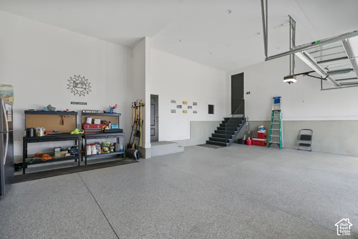 Spacious garage with epoxy flooring, high ceilings, a built-in staircase with dark treads, and a modern overhead garage door system