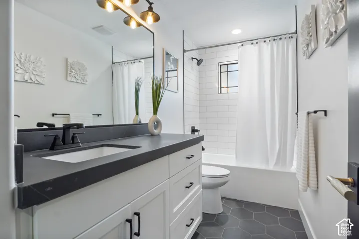 Bathroom featuring a white vanity with a dark countertop and undermount sink, black hardware, a shower-over-tub with subway tile surround, a dark hex-tile floor, and a window