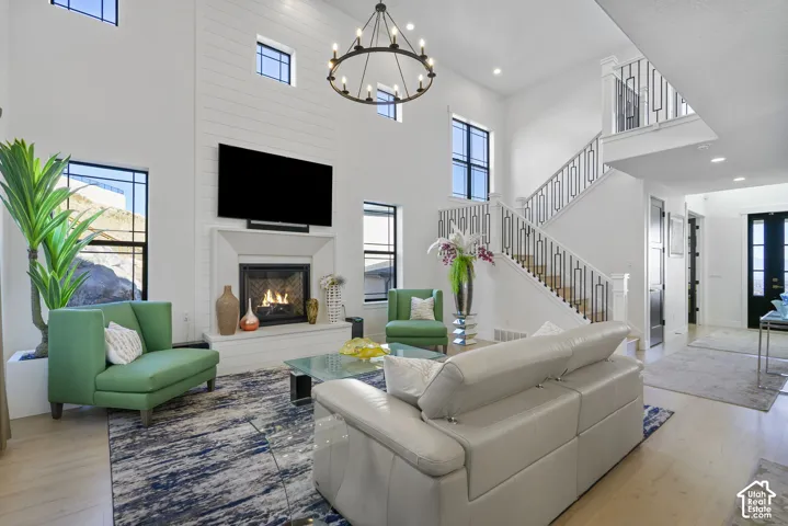 Two-story living area featuring a central fireplace with shiplap accent wall, a grand staircase with wrought iron railing, black framed windows, and light wood-finish flooring