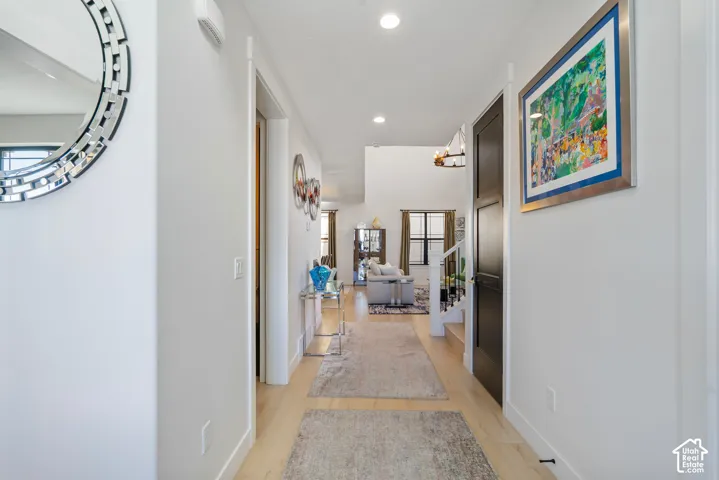Long hallway with light wood-finish flooring, white walls, and recessed lighting