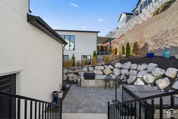 Exterior patio featuring stone pavers, a built-in outdoor grill, and a terraced rock garden with mature plantings