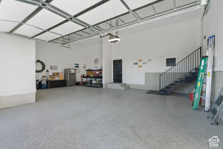 Spacious garage featuring a durable epoxy floor, an integrated staircase with wrought iron railing, a pedestrian door, and high ceilings