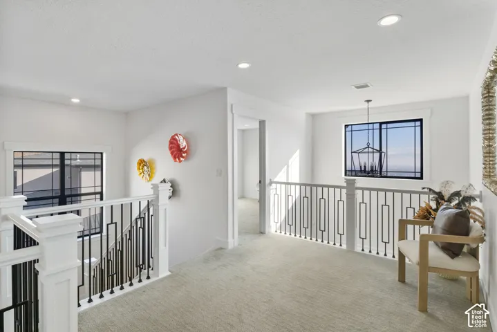 Upper-level landing featuring a white railing with black metal balusters, recessed lighting, and light gray carpeting