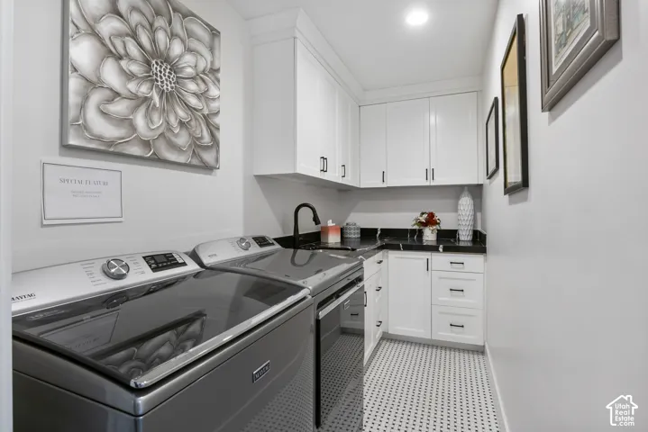 Dedicated laundry space featuring white shaker cabinetry, dark countertops, black fixtures, and mosaic floor tile