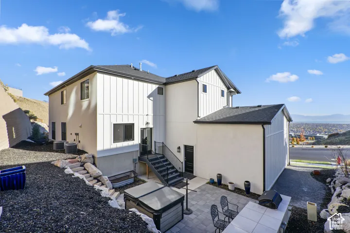 Multi-level exterior featuring white siding and black trim, a lower-level patio with pavers, a hot tub, and a built-in outdoor counter
