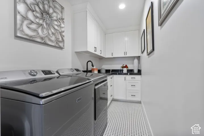 Dedicated utility space featuring white cabinetry, dark countertops, black hardware, a built-in sink with a matte black faucet, and patterned mosaic tile flooring