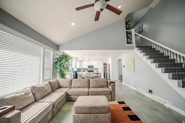 Vaulted ceiling living area featuring wood-finish flooring, a contemporary ceiling fan, and large windows with blinds