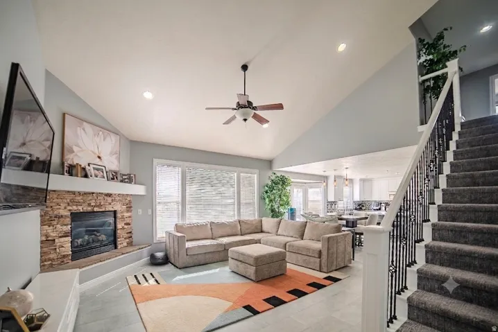 Spacious living area featuring vaulted ceilings, a stone-clad fireplace, and large windows