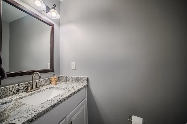 Bathroom vanity featuring a rectangular undermount sink, a granite countertop, brushed nickel faucet, and a wall-mounted mirror with overhead lighting