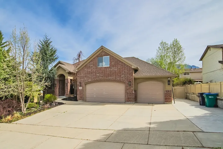 Brick and stucco exterior featuring a multi-car driveway, arched entry, and integrated two-car garage