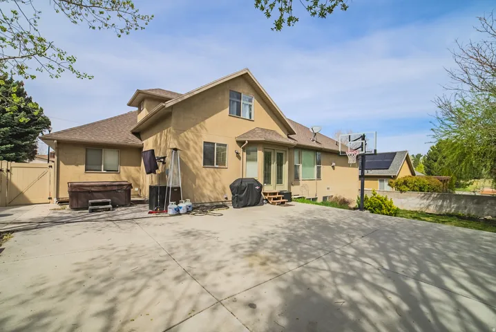 Expansive concrete patio area with a stucco exterior home featuring multiple windows, a hot tub, and a privacy fence