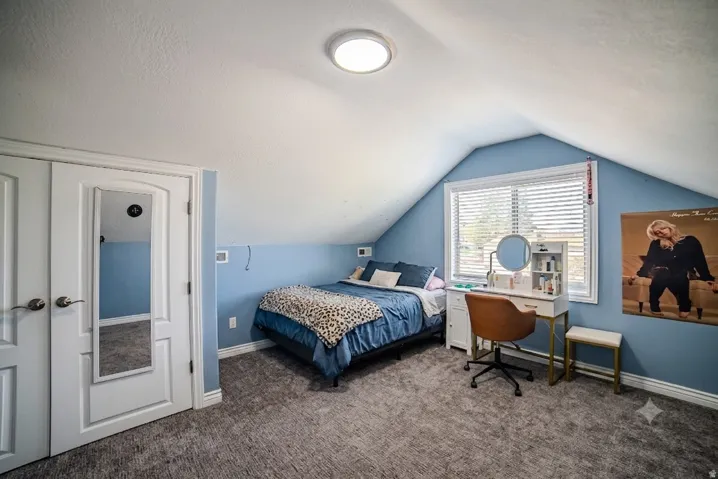 Spacious room featuring vaulted ceilings, a window with blinds, light blue walls, grey textured carpet, and white trim