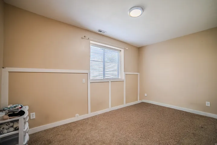 Carpeted room featuring a window with blinds, board and batten wall detailing, a flush-mount ceiling light, and neutral wall tones