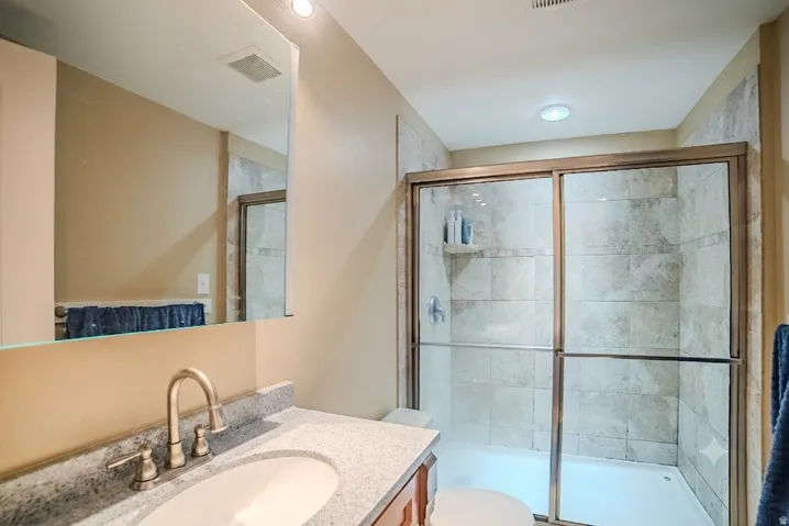 Bathroom featuring a tiled shower with sliding glass doors, a vanity with a stone-finish countertop, an undermount sink, and a framed mirror