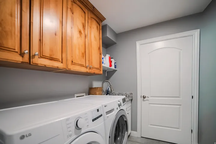 Laundry area with natural wood cabinetry, a granite-patterned countertop, and a utility sink with a chrome faucet