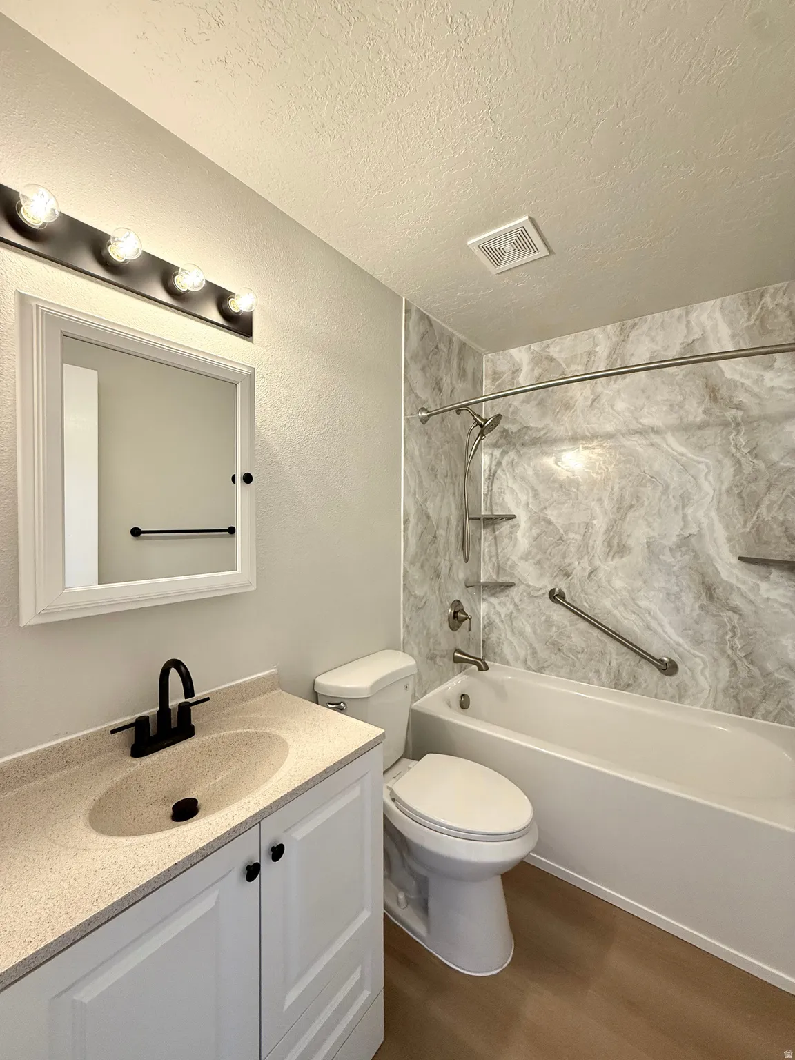 Full bathroom featuring a white vanity with a speckled countertop, integrated sink, and matte black faucet