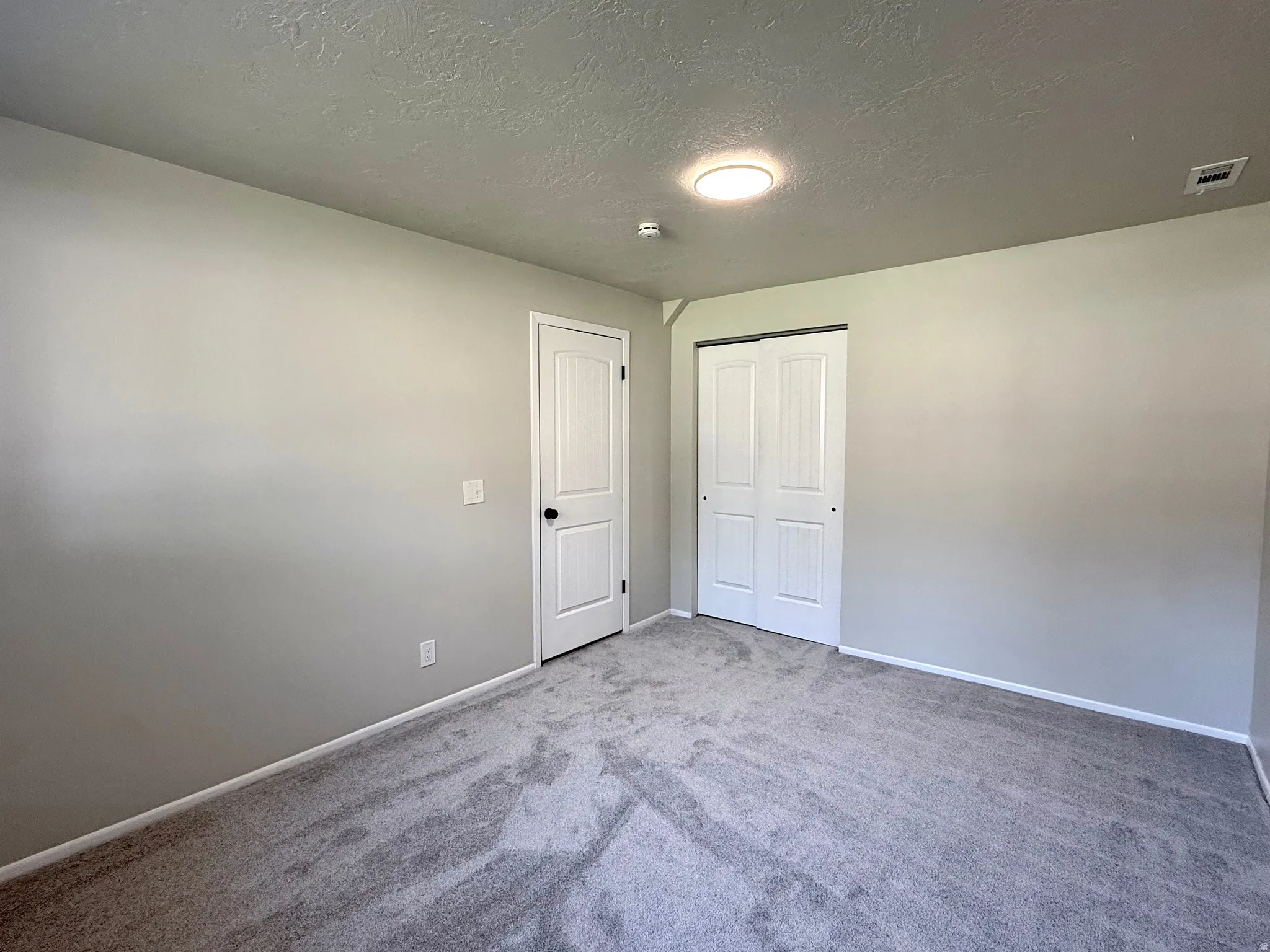 Bedroom featuring light gray wall paint, gray carpet flooring, white baseboards, and a white paneled door with black hardware
